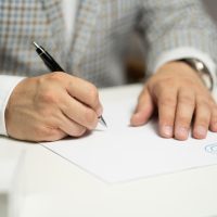编辑部内容负责人在开放式办公区对着双屏整理文档要点，桌面堆着标注过的打印材料，光线明亮